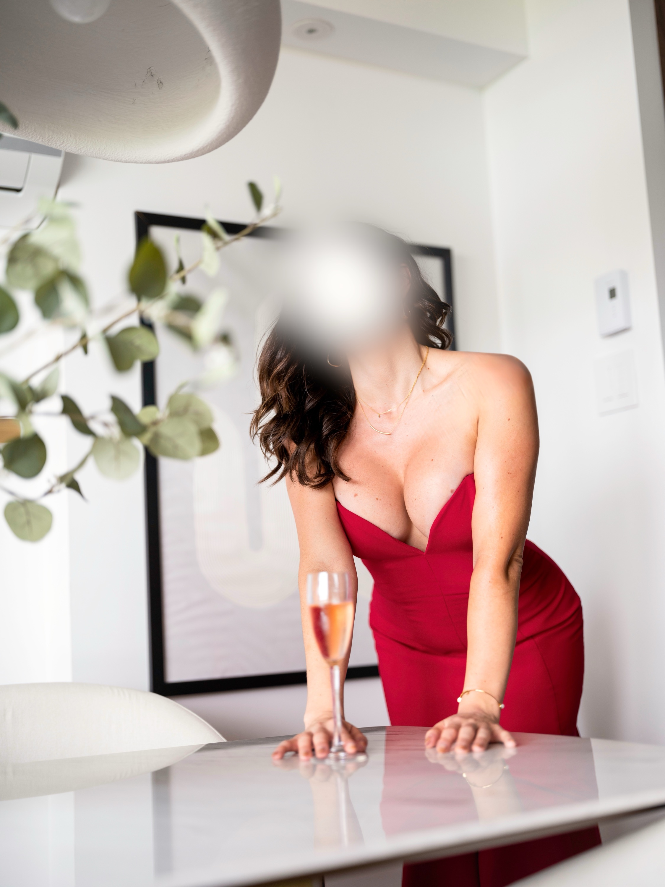 Woman in a red dress leaning over a table beside a glass of champagne